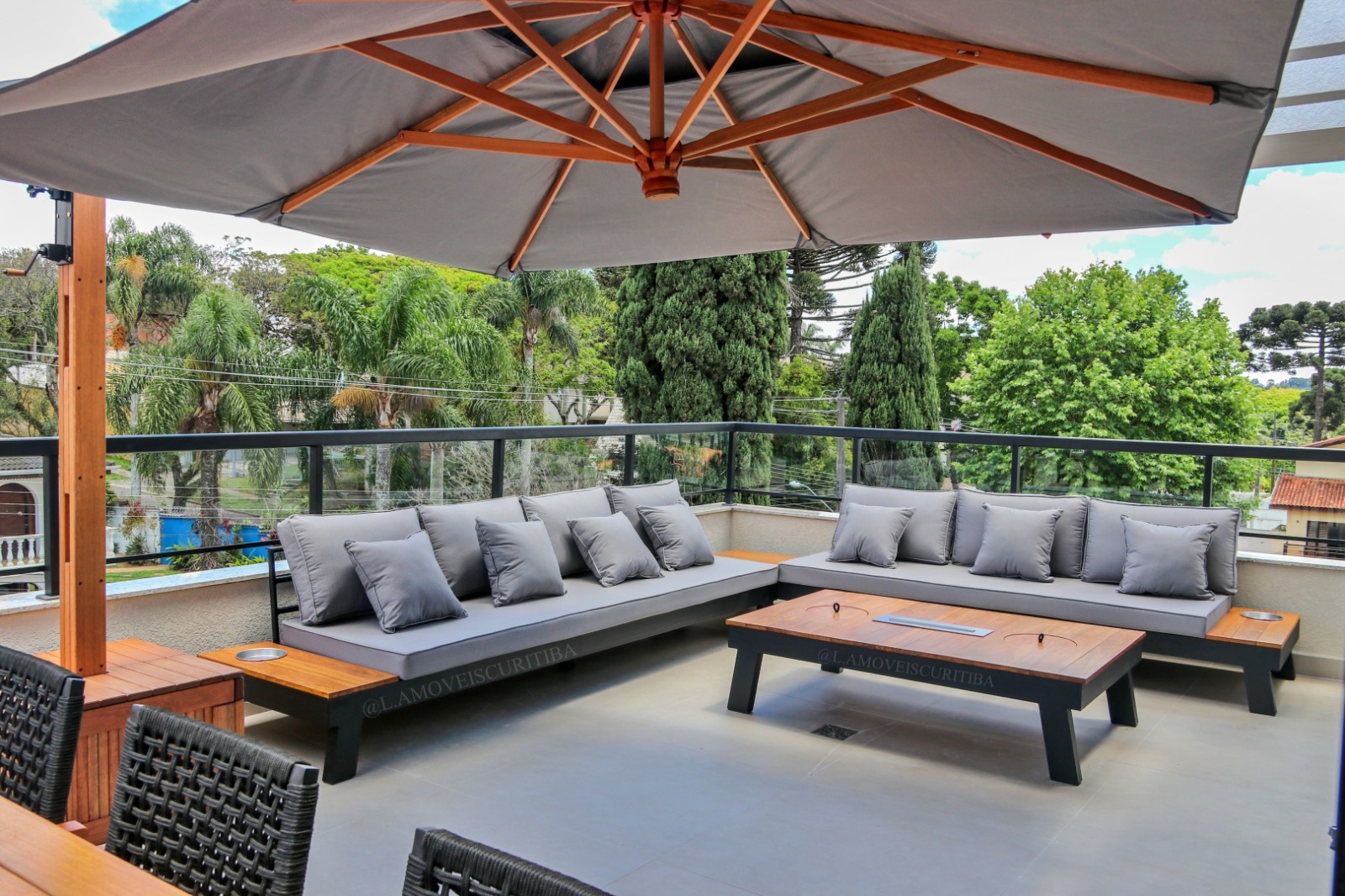 Lounge outdoor de alto padrão com sofás modulares sob ombrelone em varanda com vista para a mata