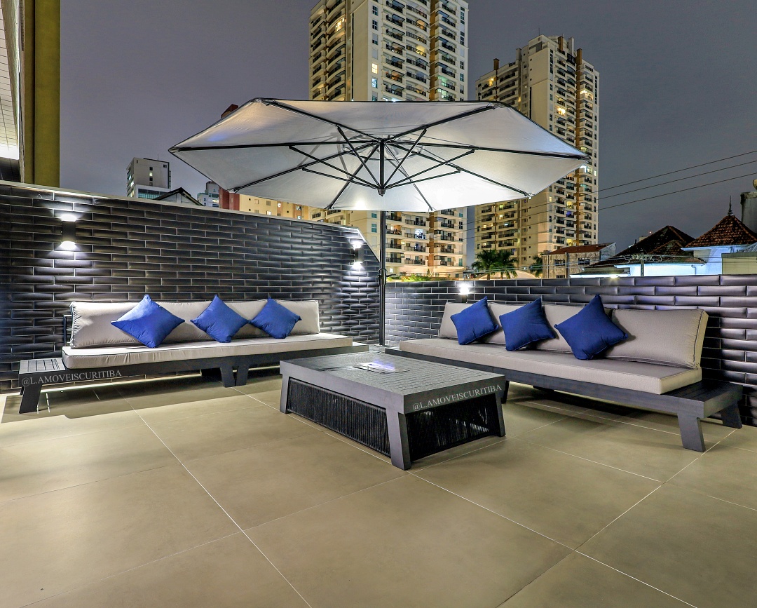 Rooftop iluminado à noite com sofás outdoor e ombrelone
