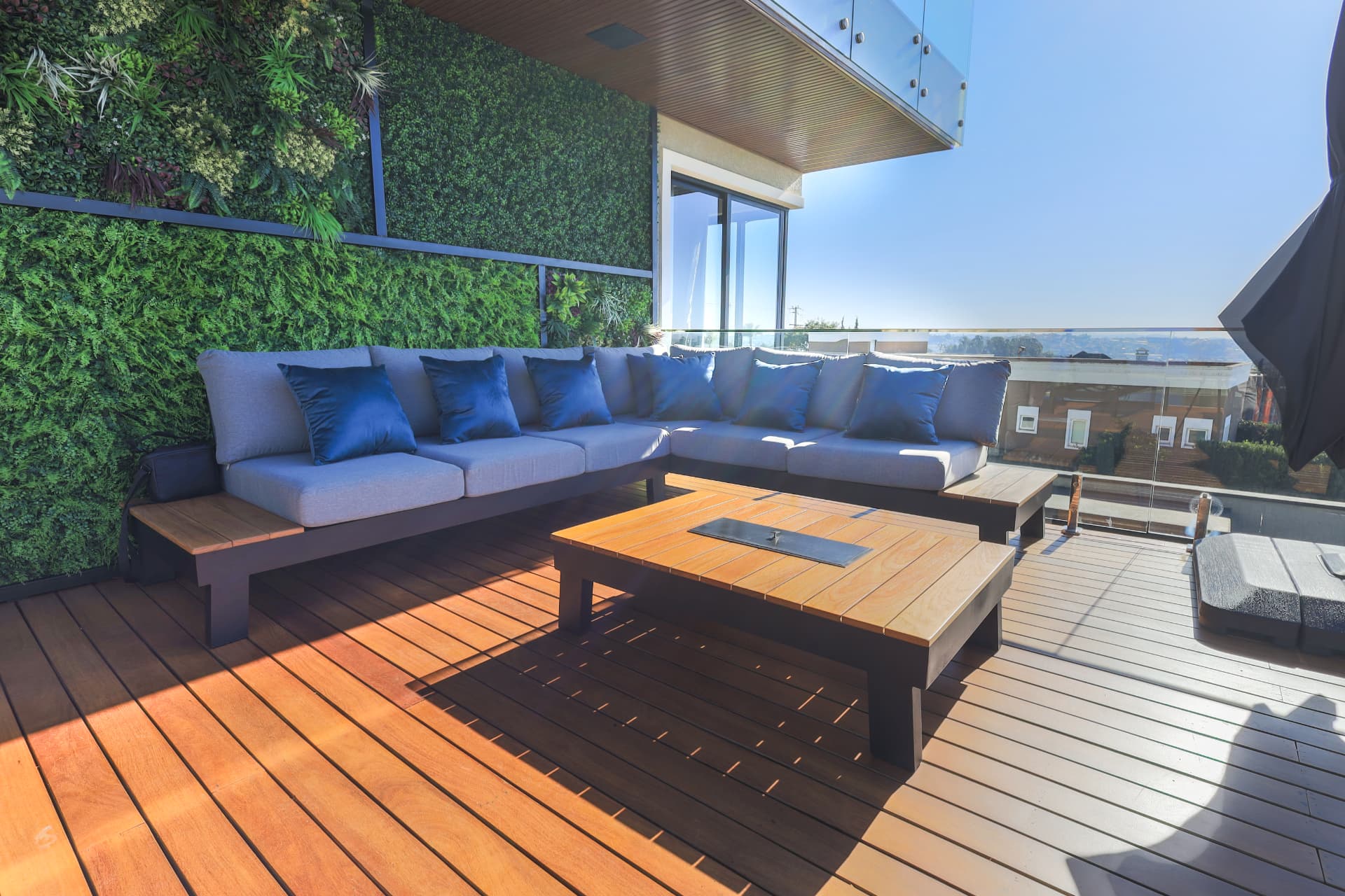 Sofá em L em rooftop de alto padrão com deck de madeira, mesa central e parede verde